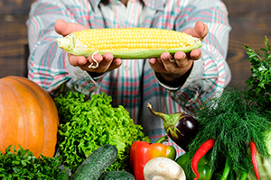 Farm stand worker presents an ear of corn